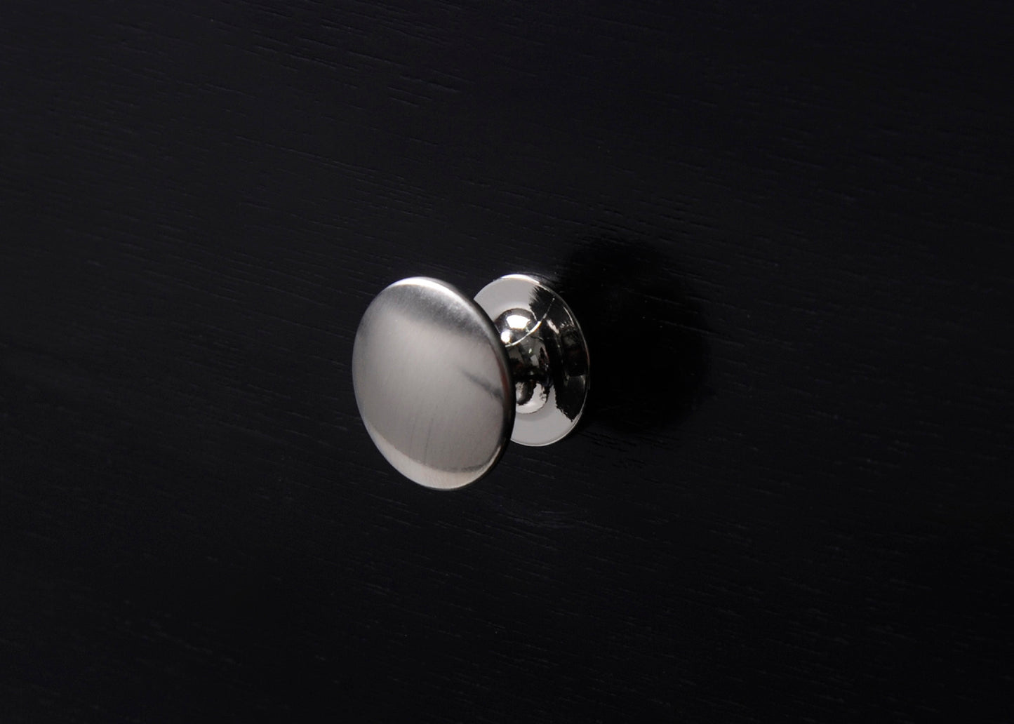 Brushed nickel cabinet knob with a round flat pull on a black surface