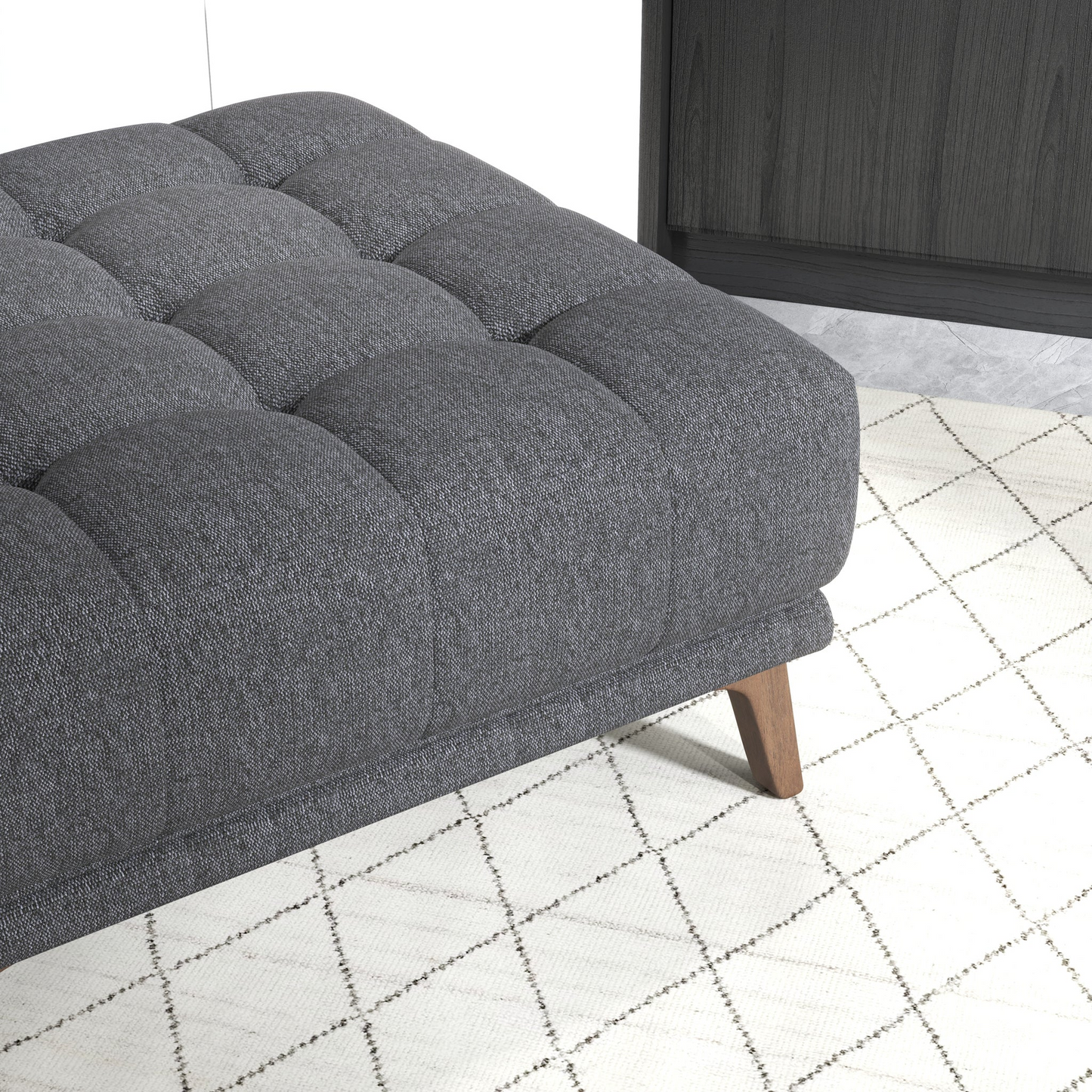 Dark grey tufted upholstered ottoman with wooden legs on a diamond patterned rug