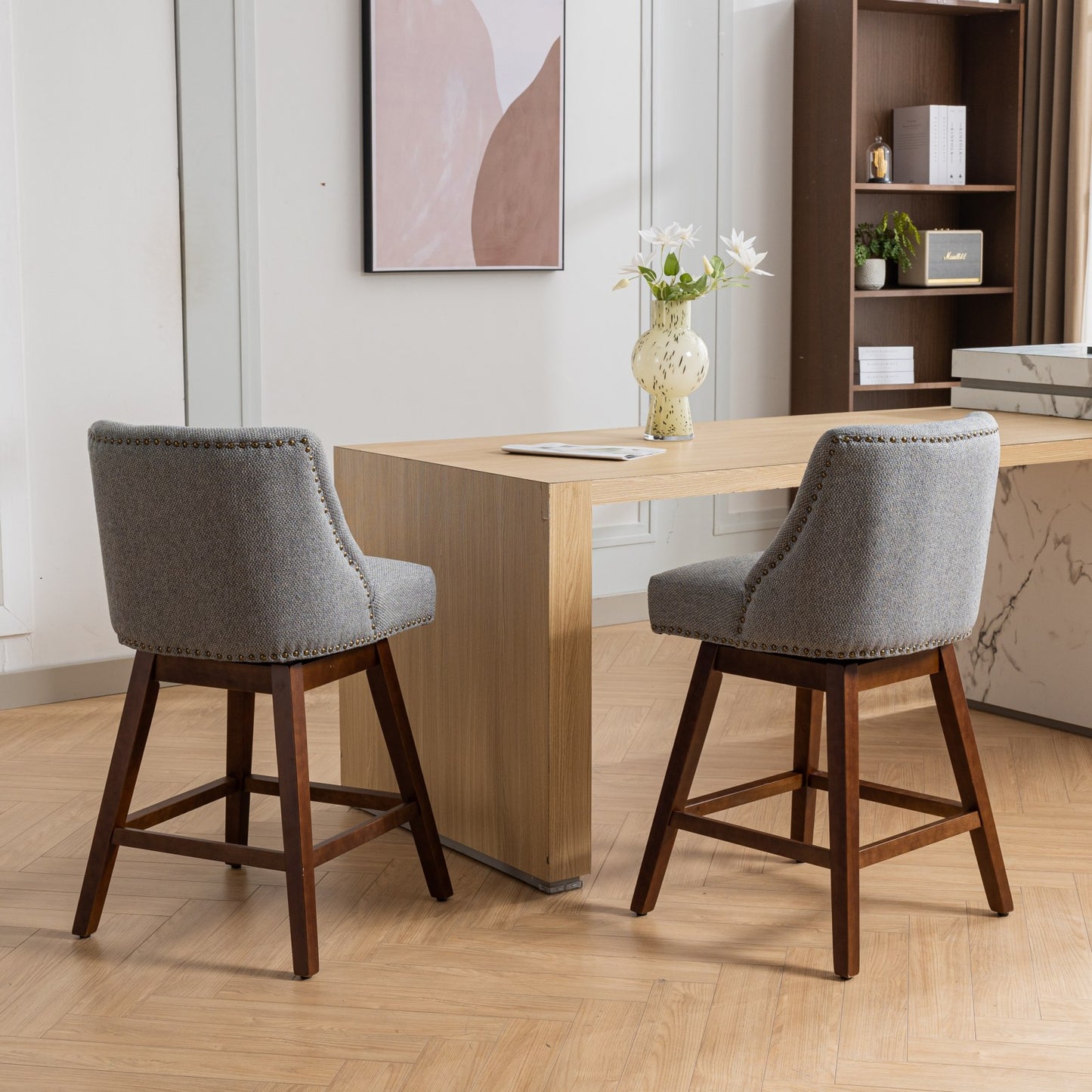 Grey upholstered swivel bar stool with brass nailhead trim and dark wood legs