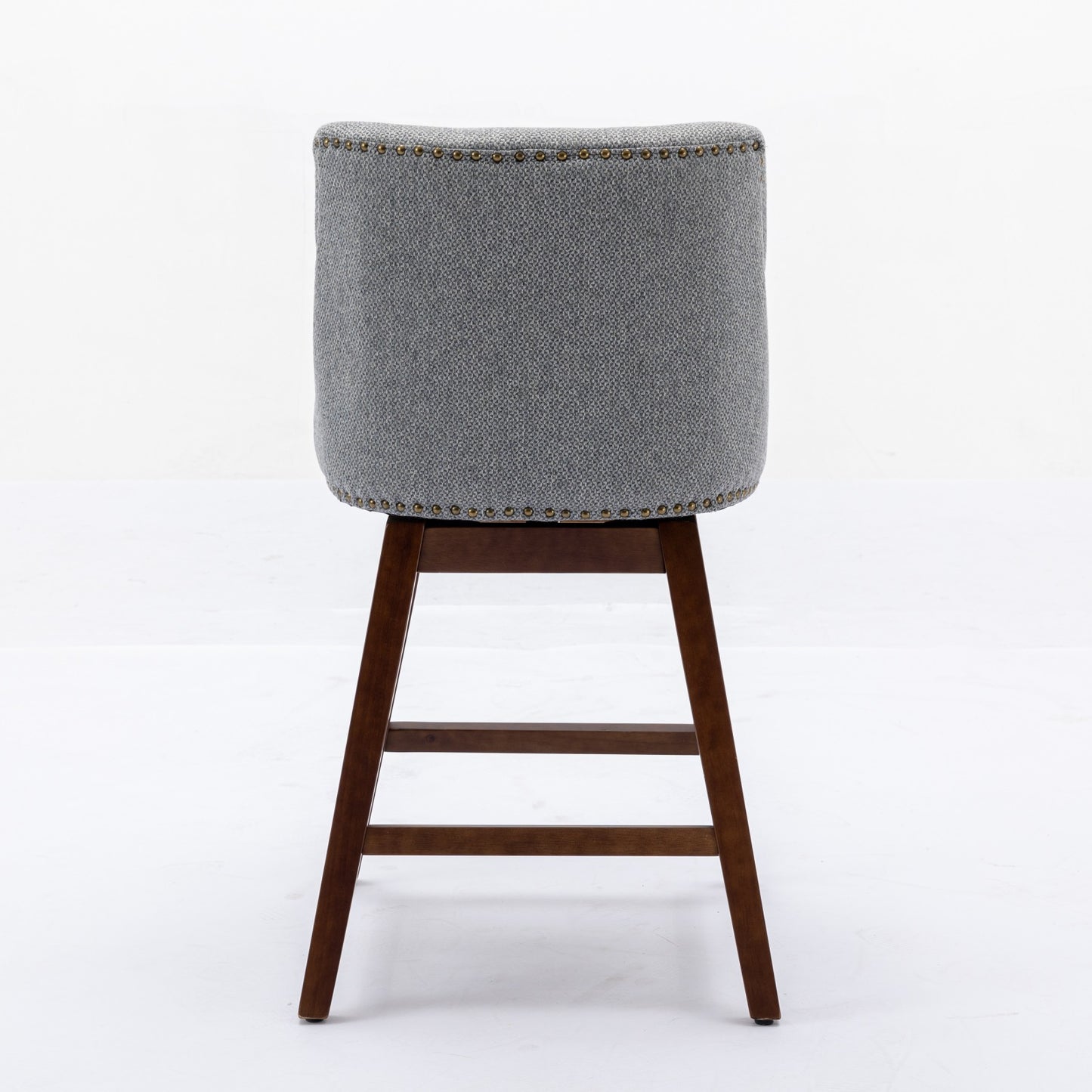 Back view of a grey upholstered swivel bar stool with brass nailhead trim and dark wood legs