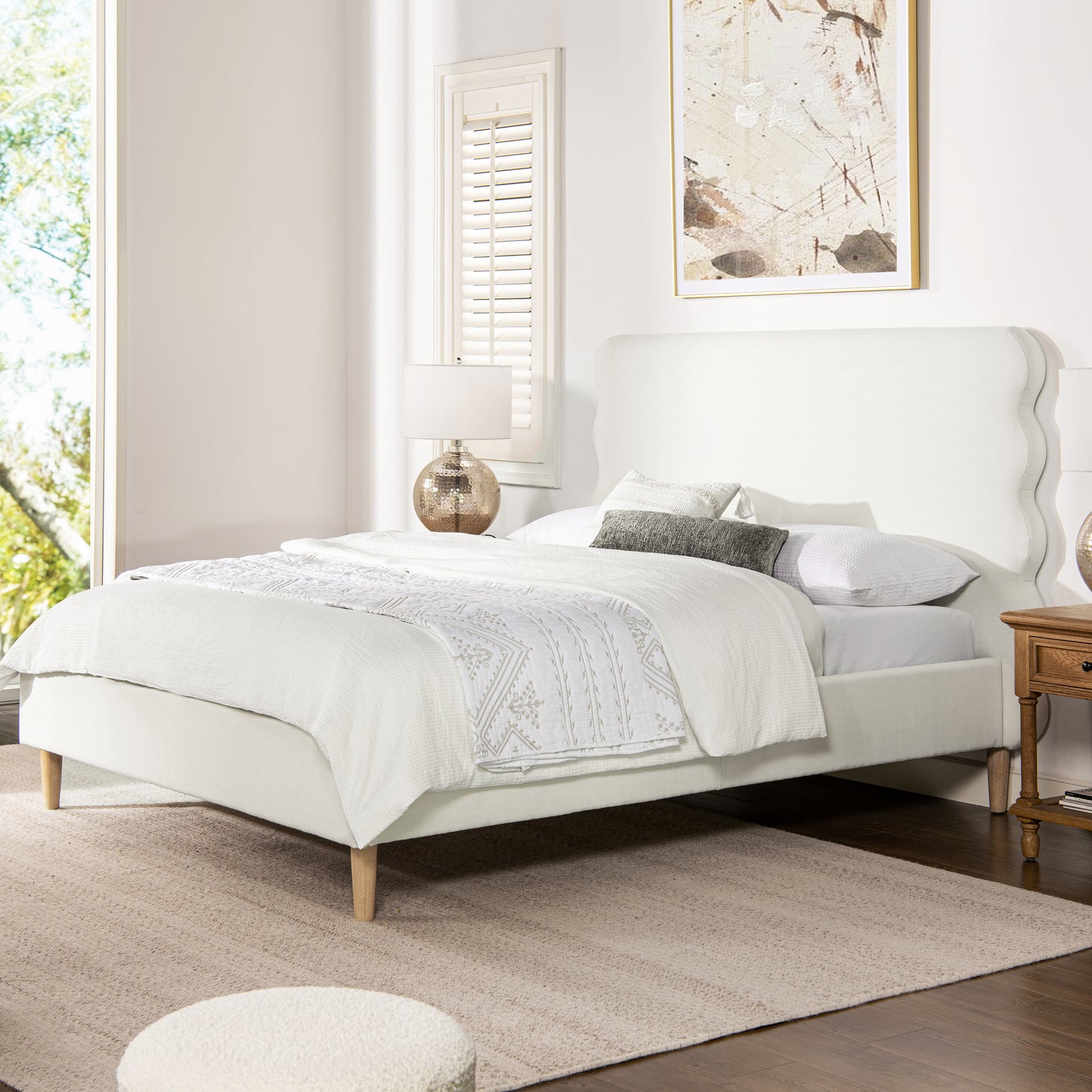 White fabric bed frame with a scalloped headboard and wooden legs styled with white bedding