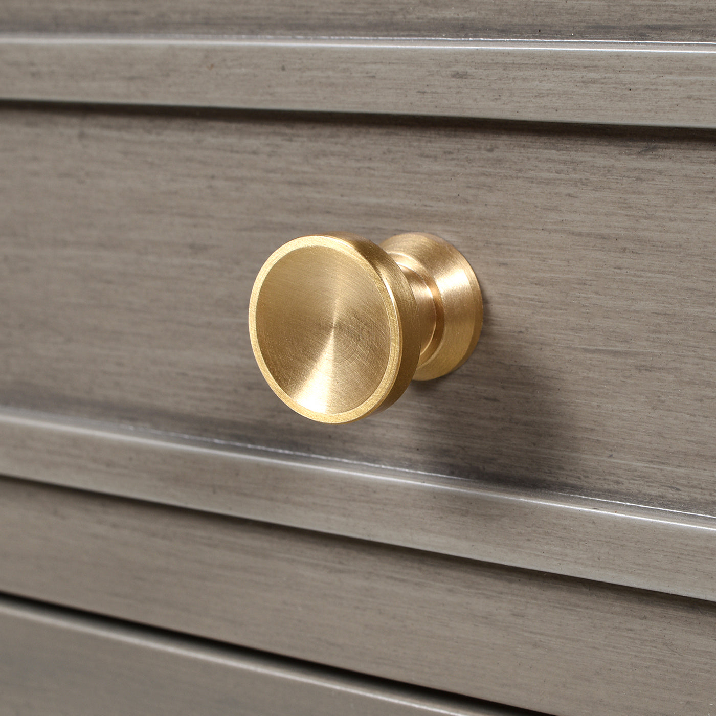 Round brushed brass cabinet knob with minimalist design on grey wood drawer