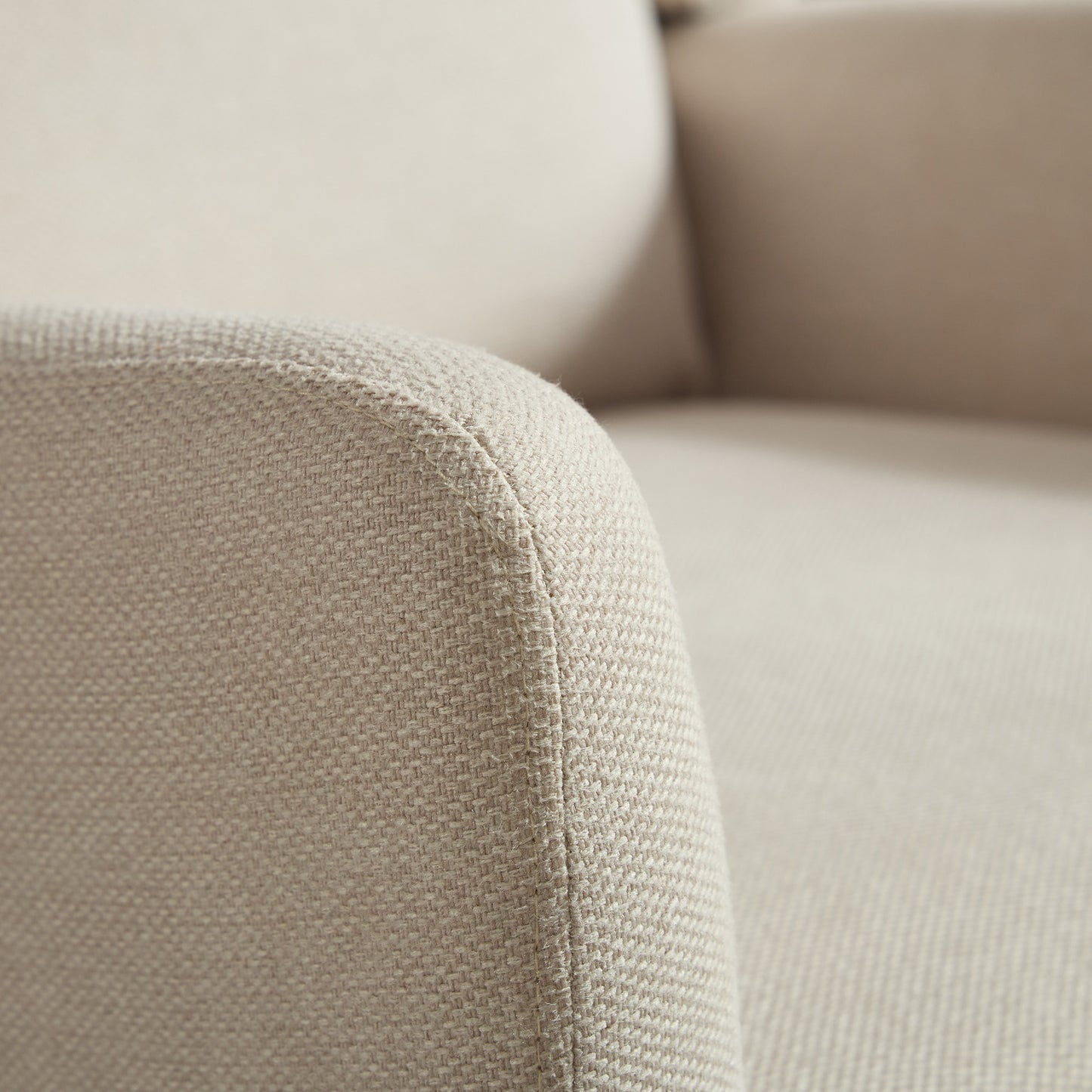 Closeup of a beige textured fabric armchair armrest with visible stitching detail