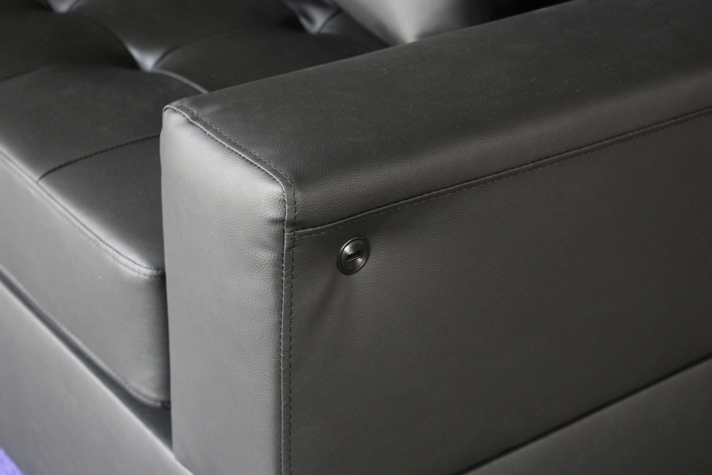 Black faux leather sofa armrest with detailed stitching and a circular metal accent