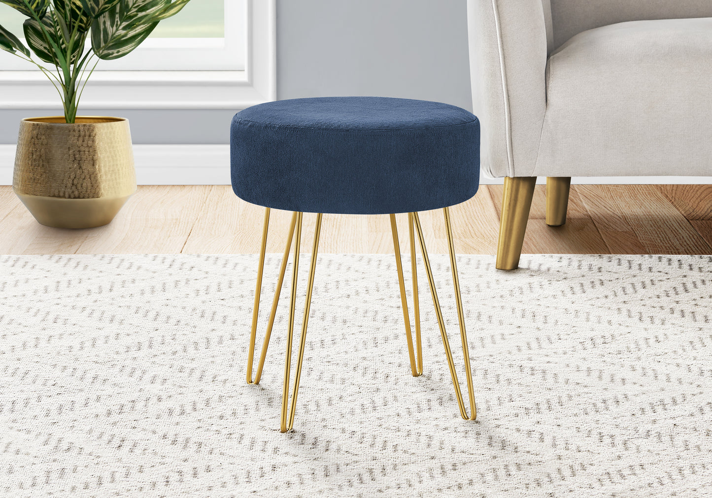 Round navy blue fabric ottoman with gold hairpin legs on patterned rug