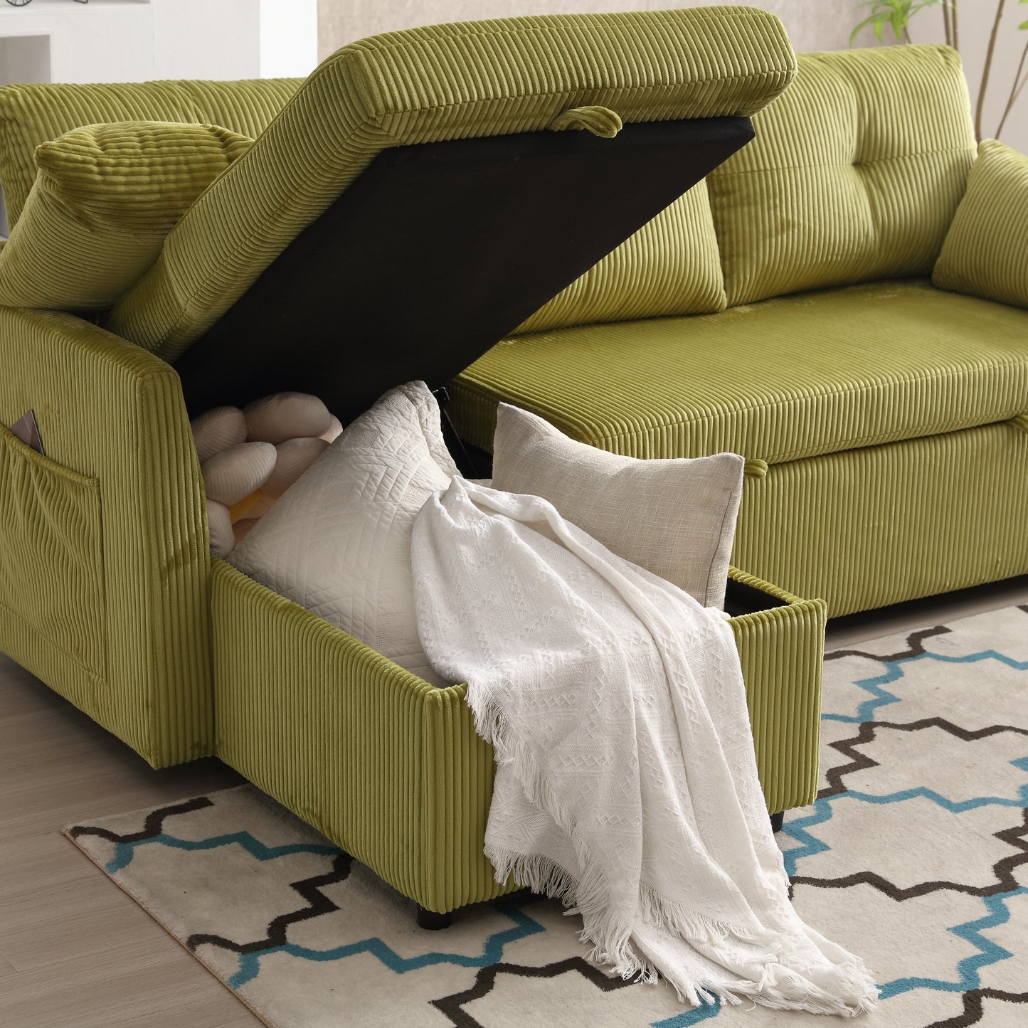 Green corduroy sofa with open storage compartment showing pillows and throw blanket