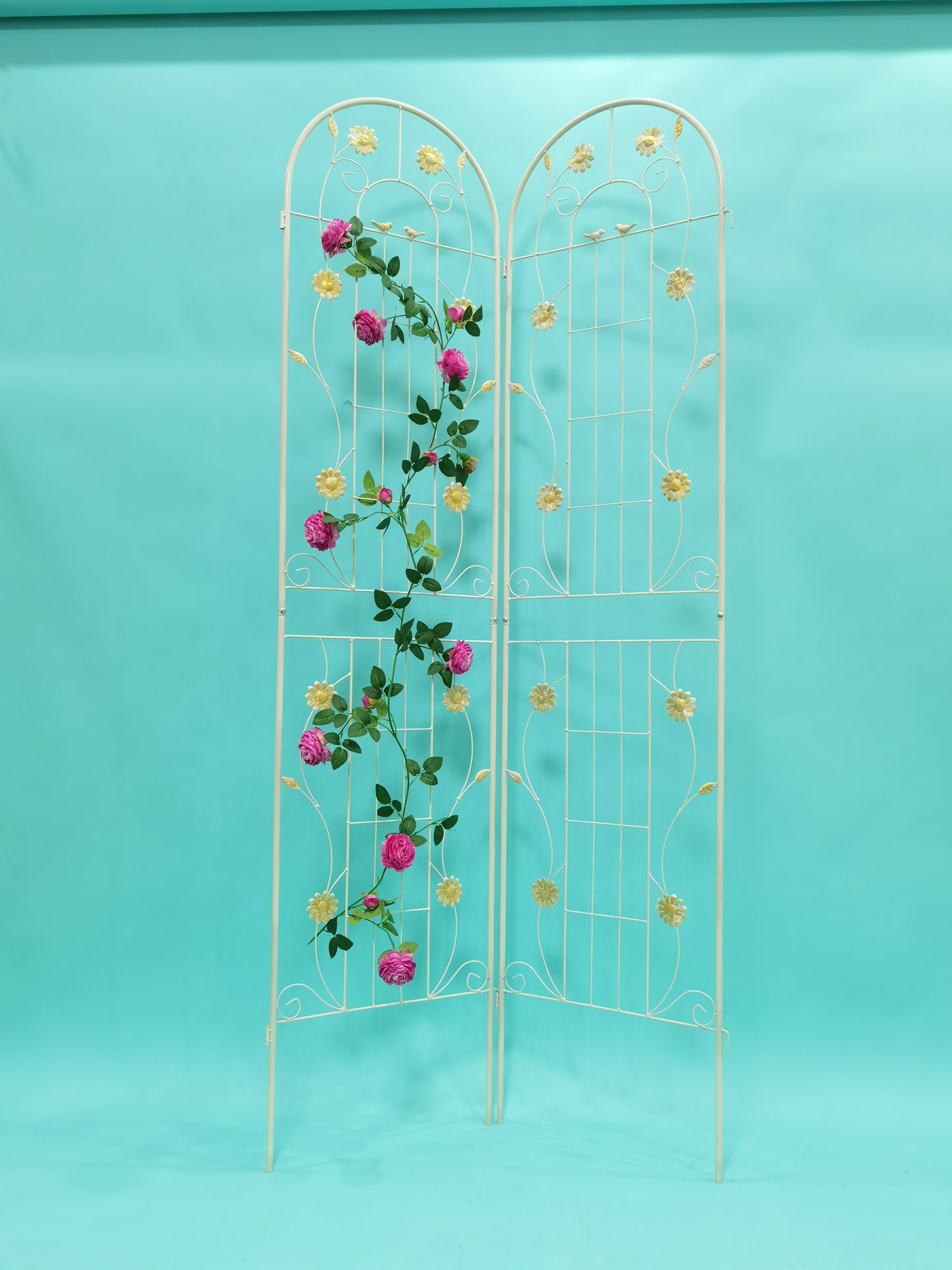 Ornate white metal garden trellis adorned with pink roses and yellow daisies