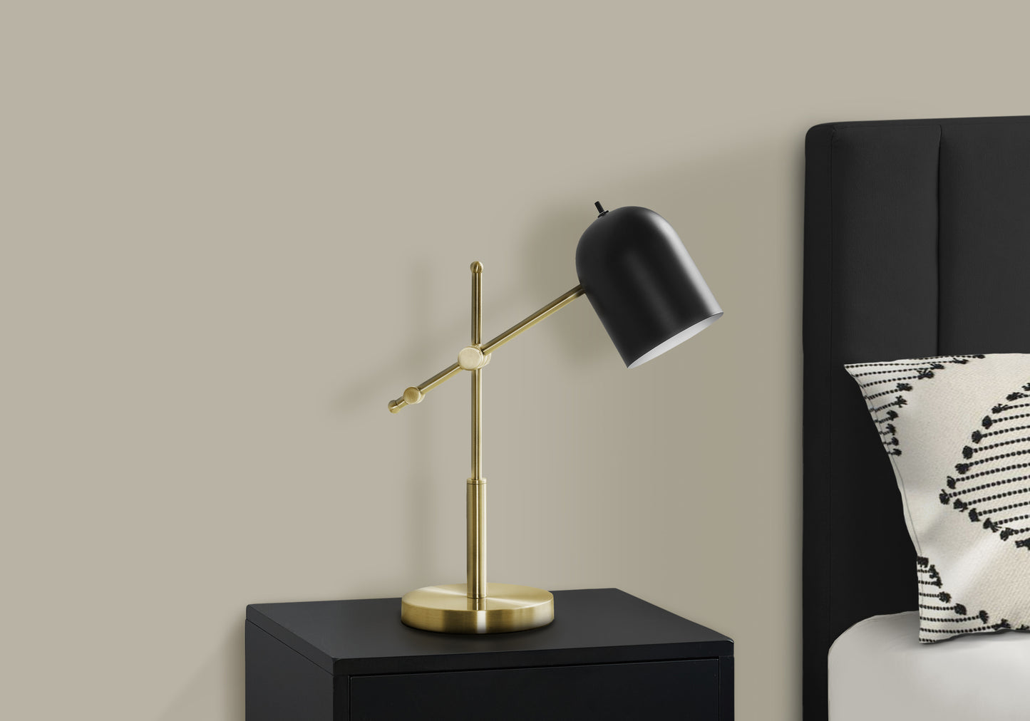 Adjustable desk lamp with black shade and brass finish on black nightstand