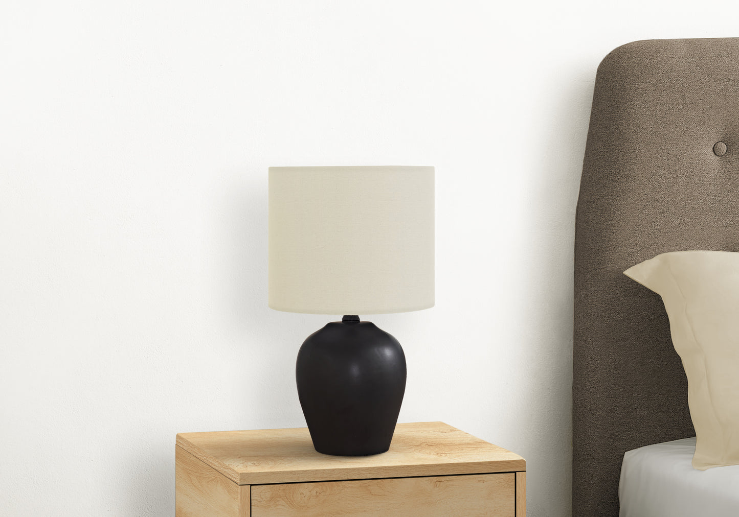 Black ceramic table lamp with cream shade on a light wood nightstand