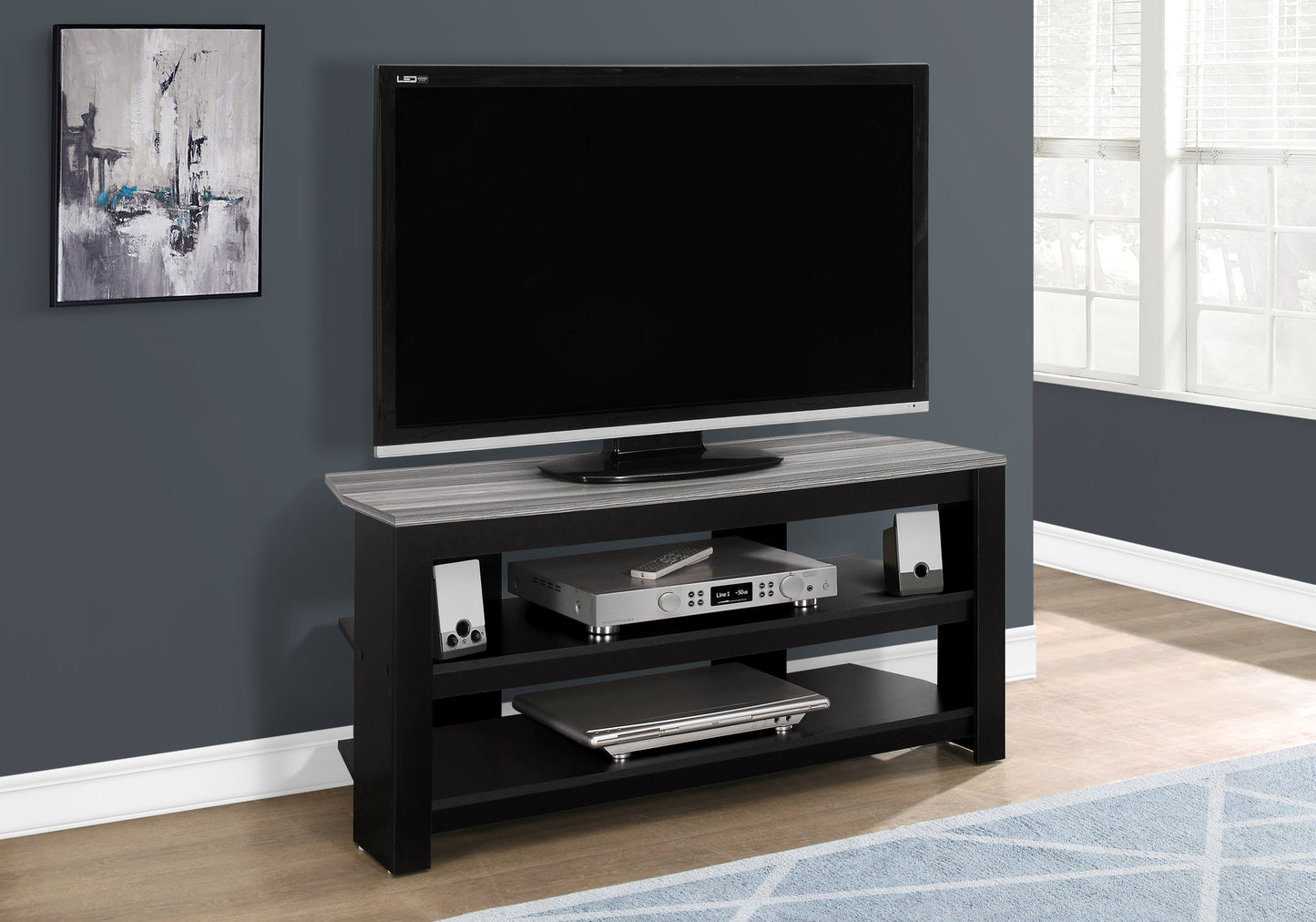 Black media console with gray wood grain top holding TV receiver DVD player and speakers