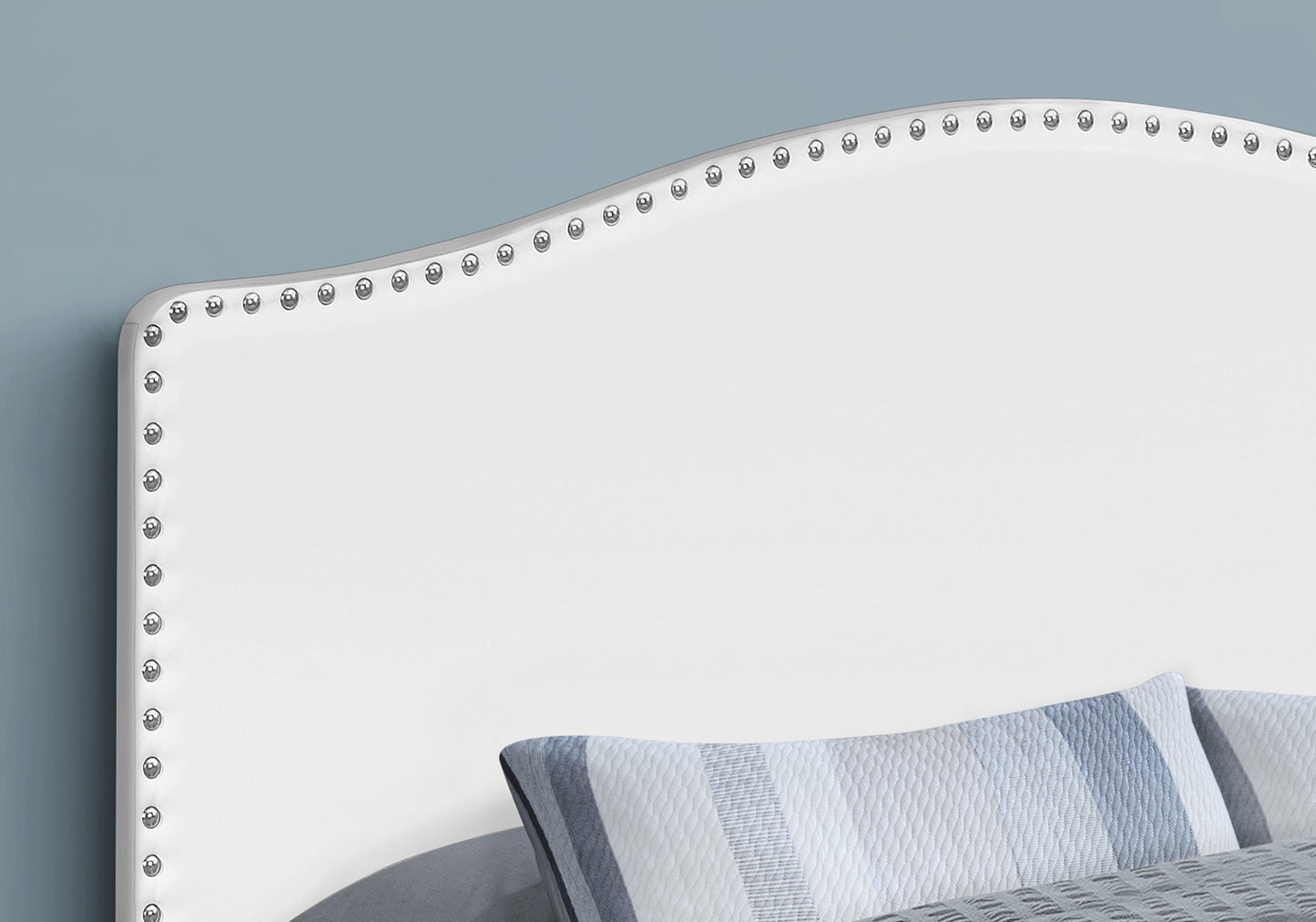White upholstered headboard with silver nailhead trim and blue striped pillows