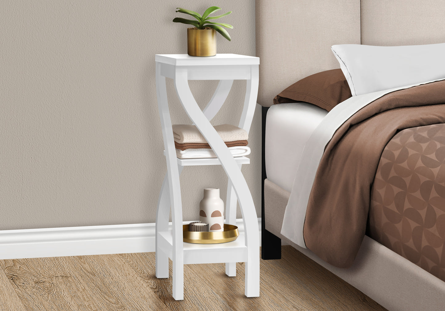 White modern tiered accent table with curved legs holding folded linens and decorative vase