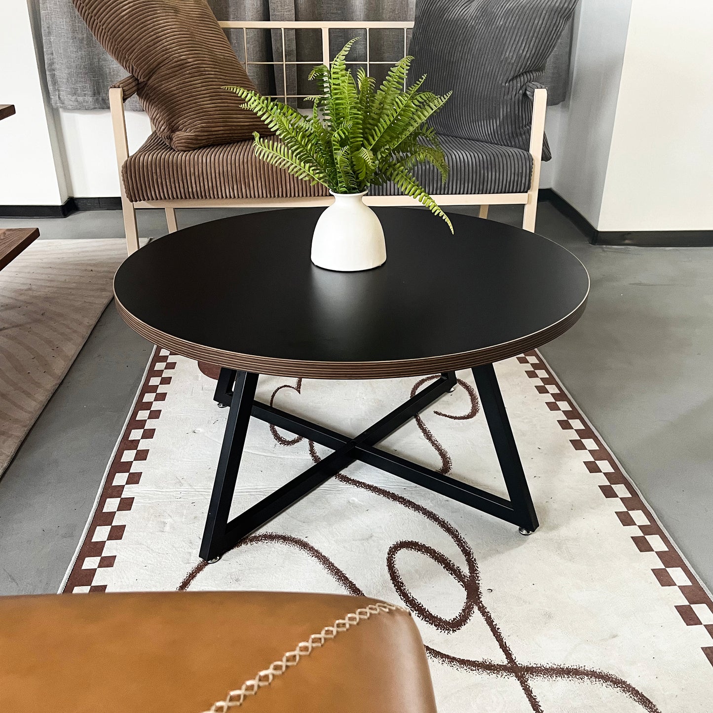 Modern black round coffee table with black metal Xframe legs and a faux fern centerpiece