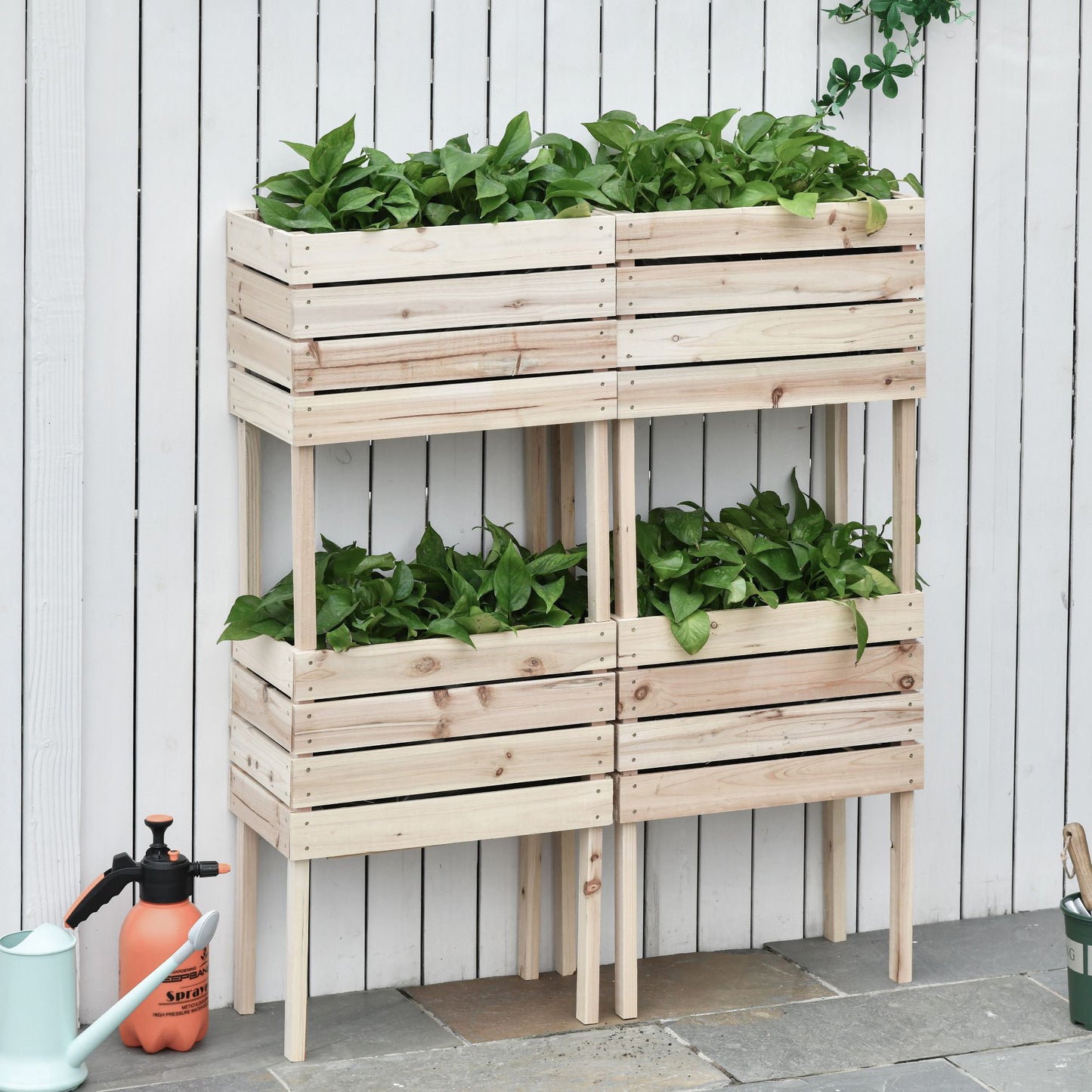 Wooden tiered planter box with lush green plants and gardening tools nearby