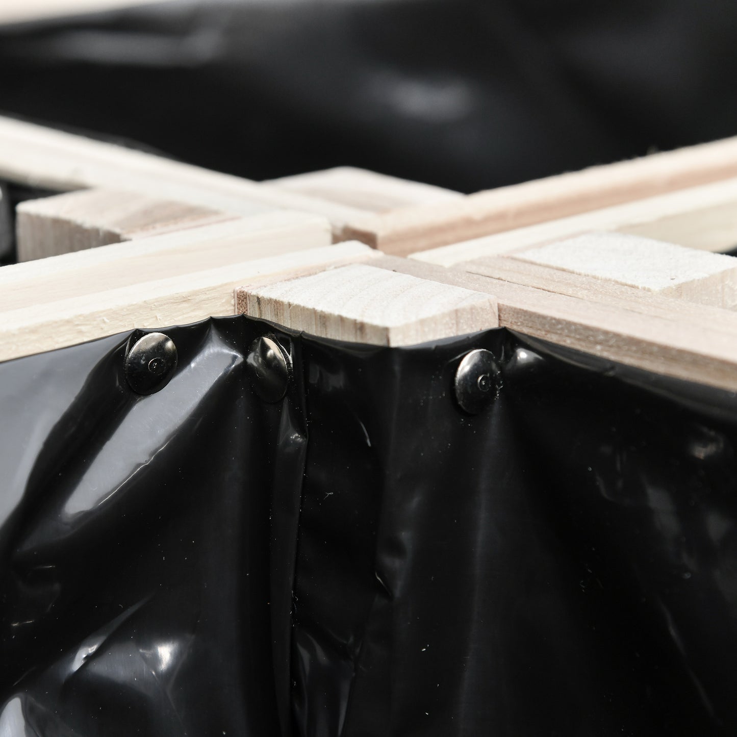 Closeup of assembled wooden raised garden bed frame with black liner secured by metal rivets