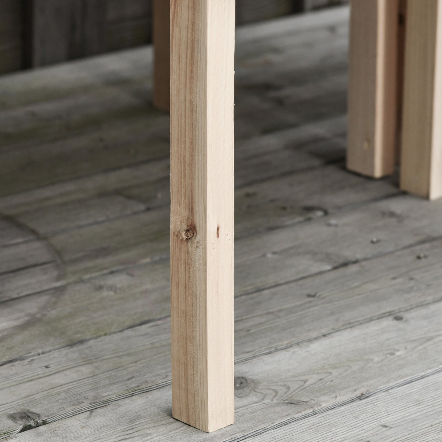 Close up of a light wood table leg on a grey wooden deck showing natural grain
