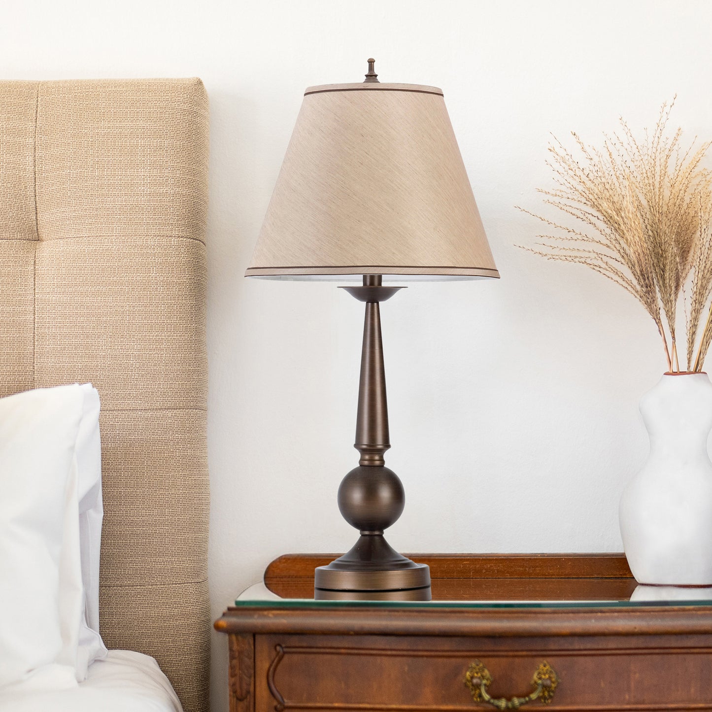 Bronze bedside lamp with a tan fabric shade featuring a decorative pedestal base