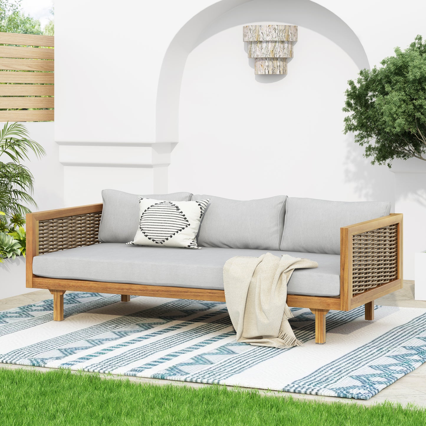 Outdoor acacia wood sofa with light grey cushions and woven rattan sides