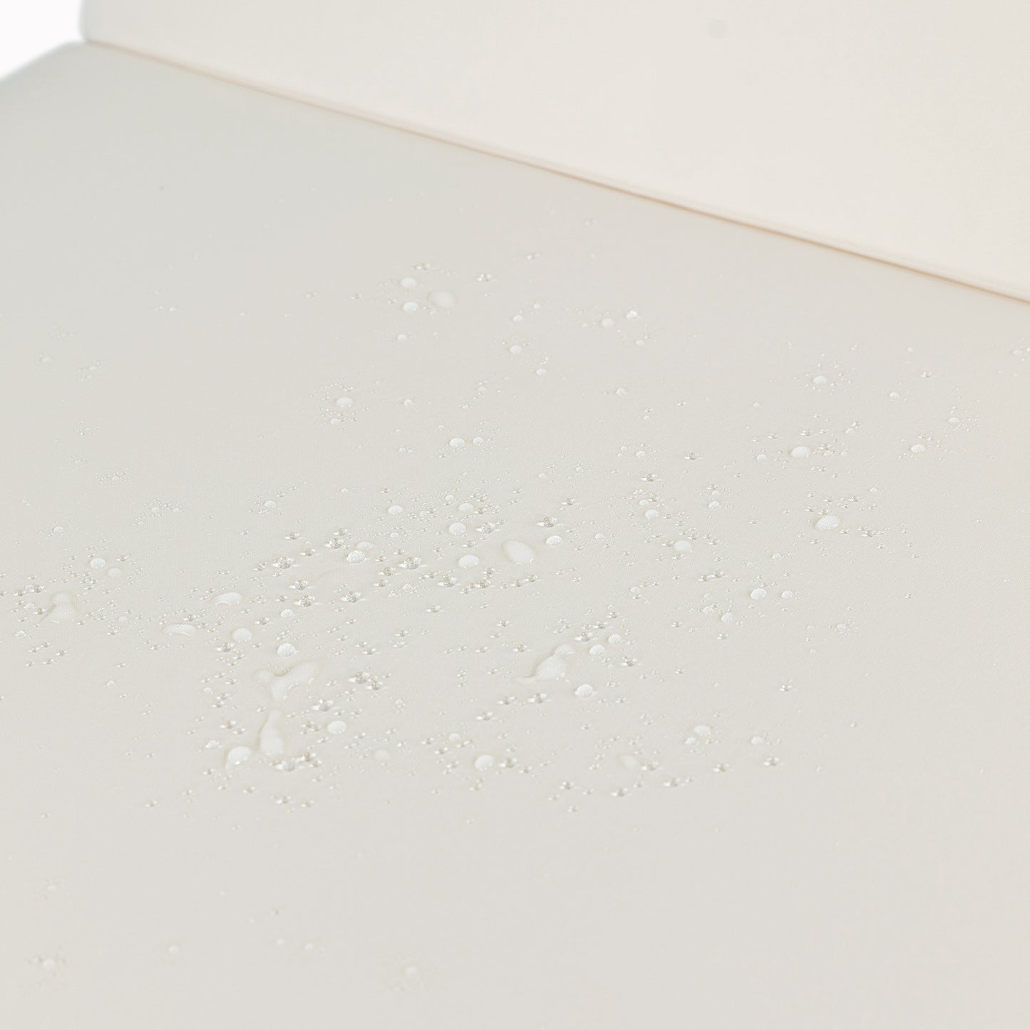 Closeup of creamcolored fabric with water droplets demonstrating its waterrepellent quality