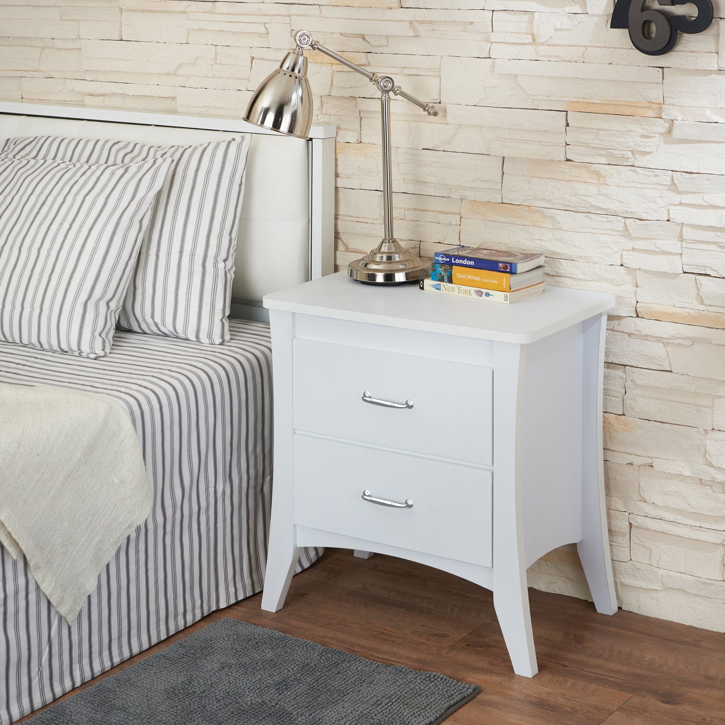 White wooden bedside table with two drawers and silver handles beside a bed