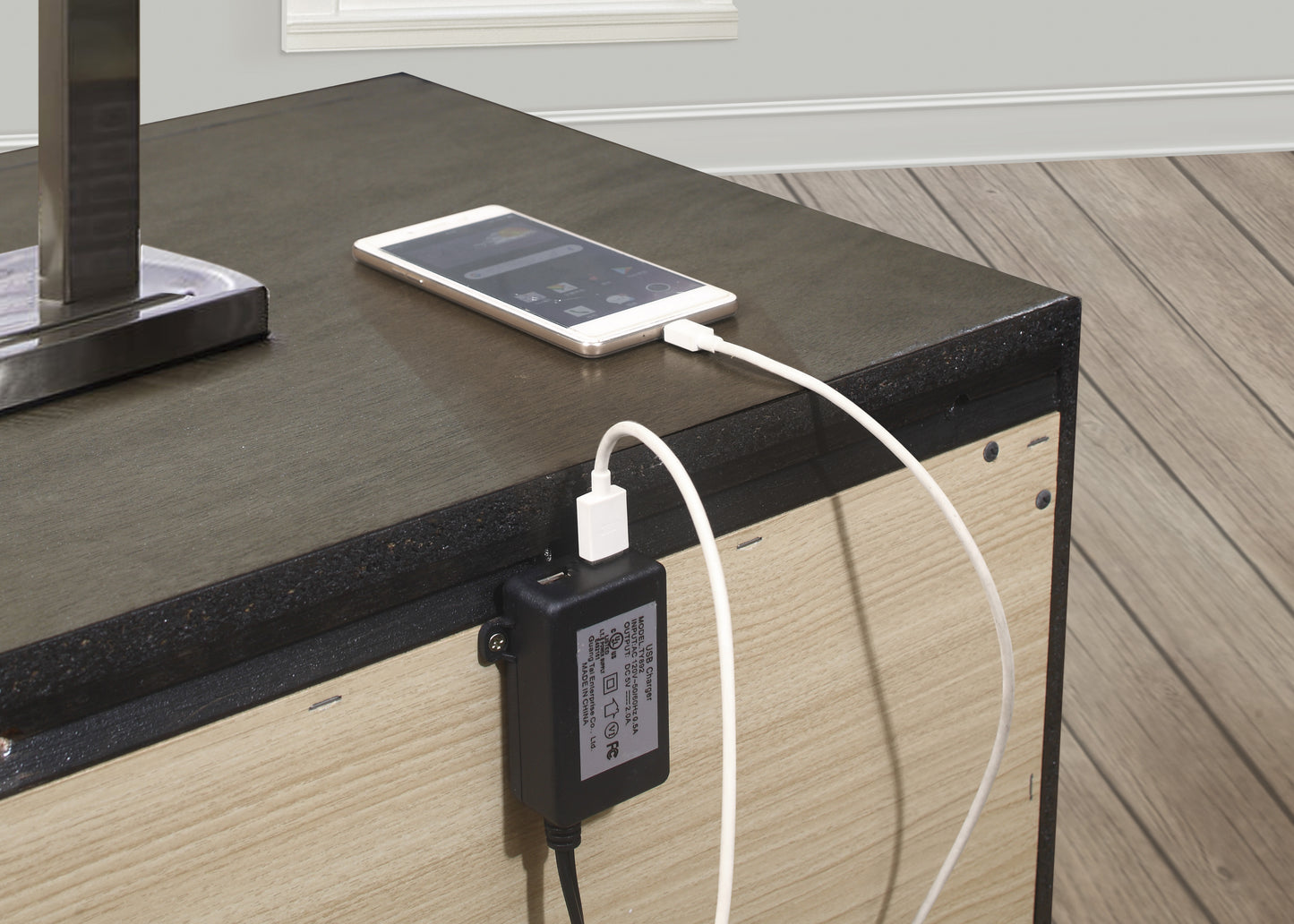White smartphone charging via USB power adapter attached to a dark wood table