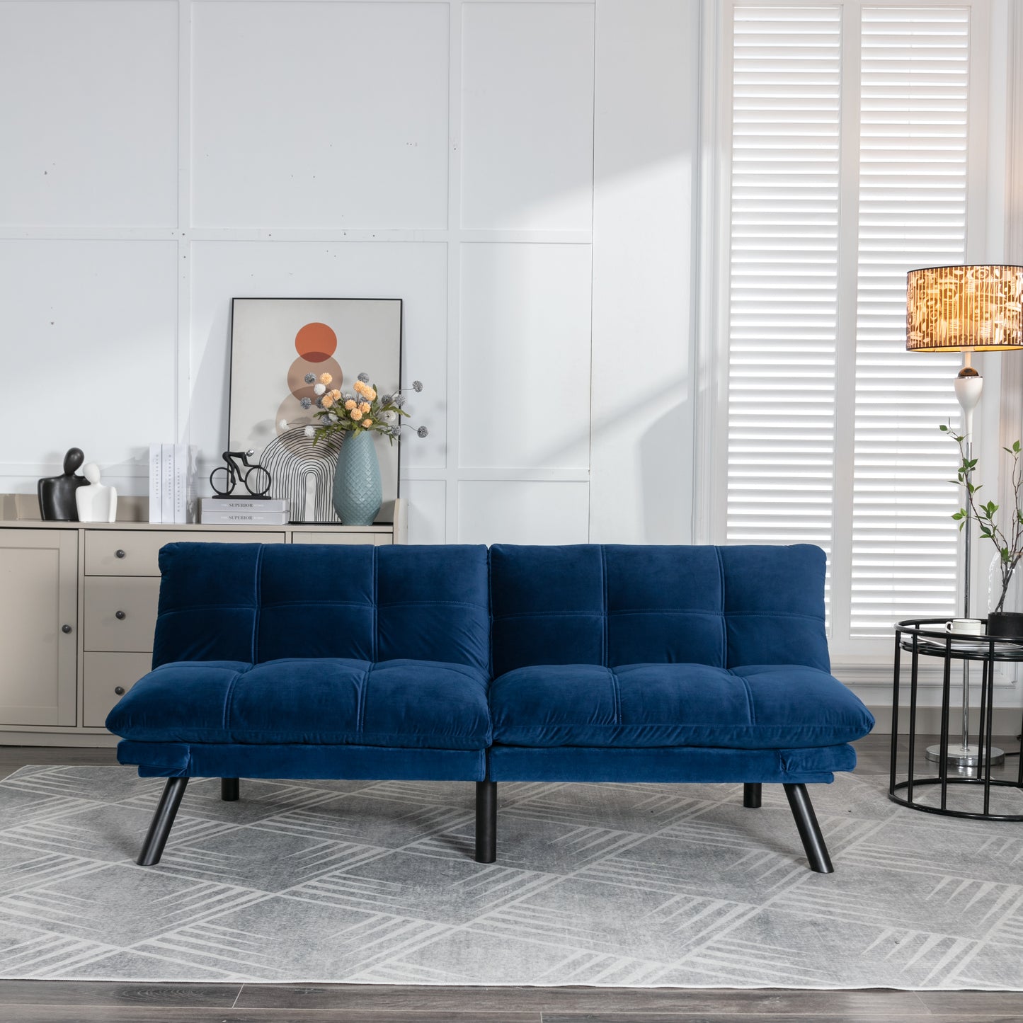 Plush velvet futon in deep navy blue featuring button tufting and sleek black legs perfect for small spaces