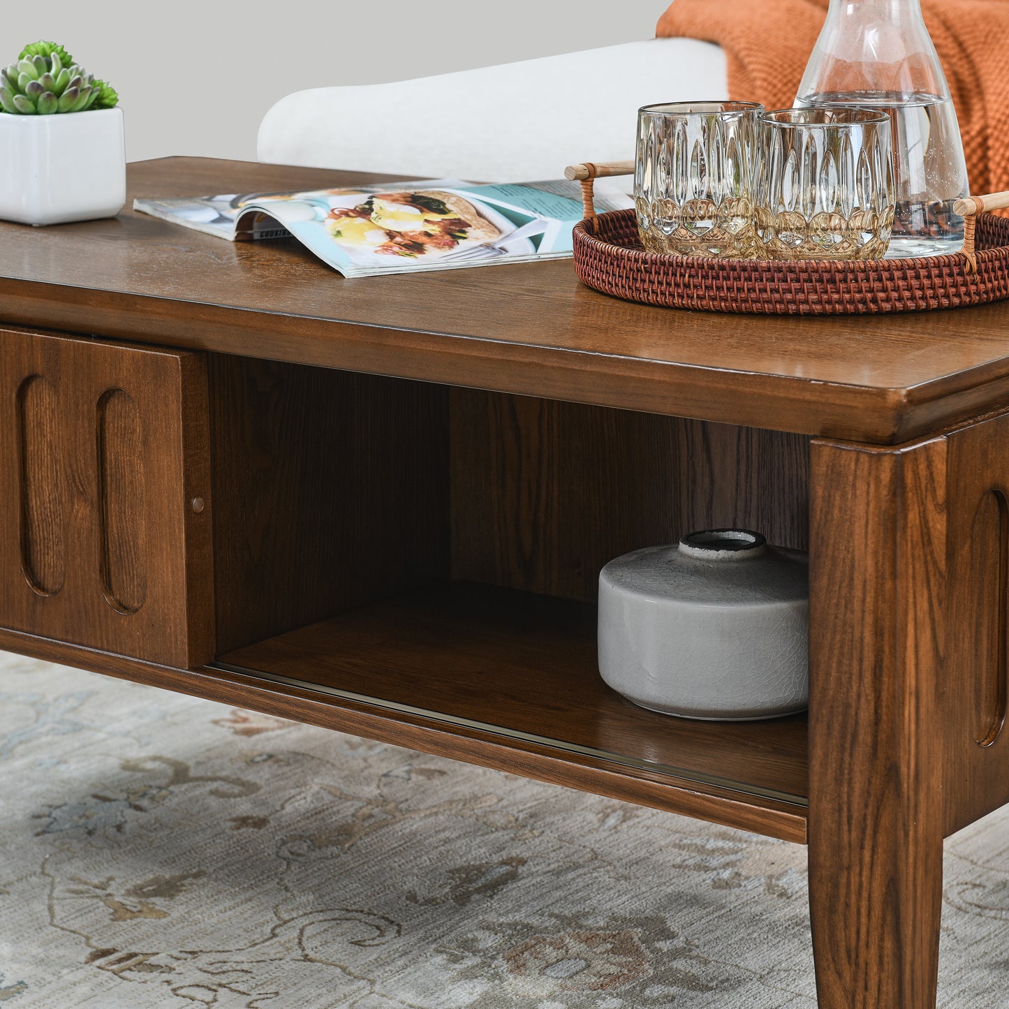 Wooden coffee table with sliding door and open shelf featuring a magazine and succulent