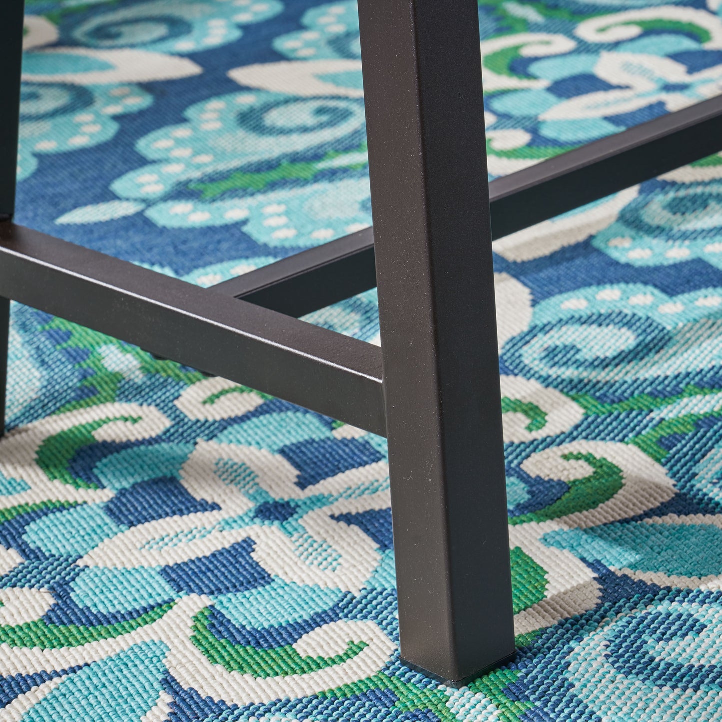 Dark metal table leg on a blue green and white floral outdoor rug