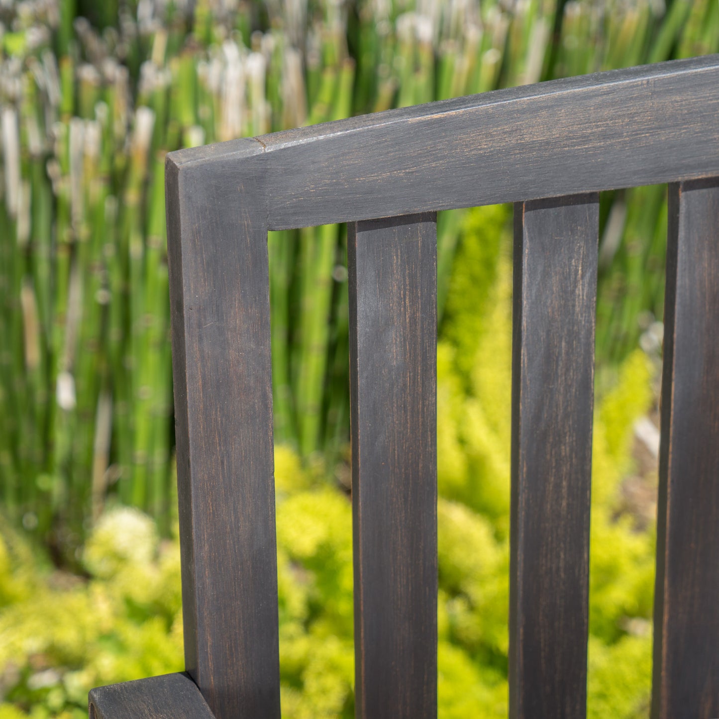 Dark wood outdoor bench slat detail with blurred green foliage background