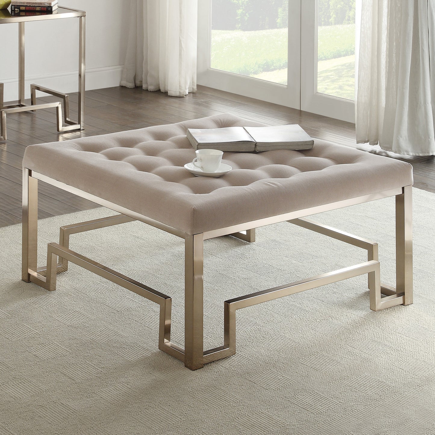 Tufted beige upholstered ottoman with a modern geometric brushed nickel base