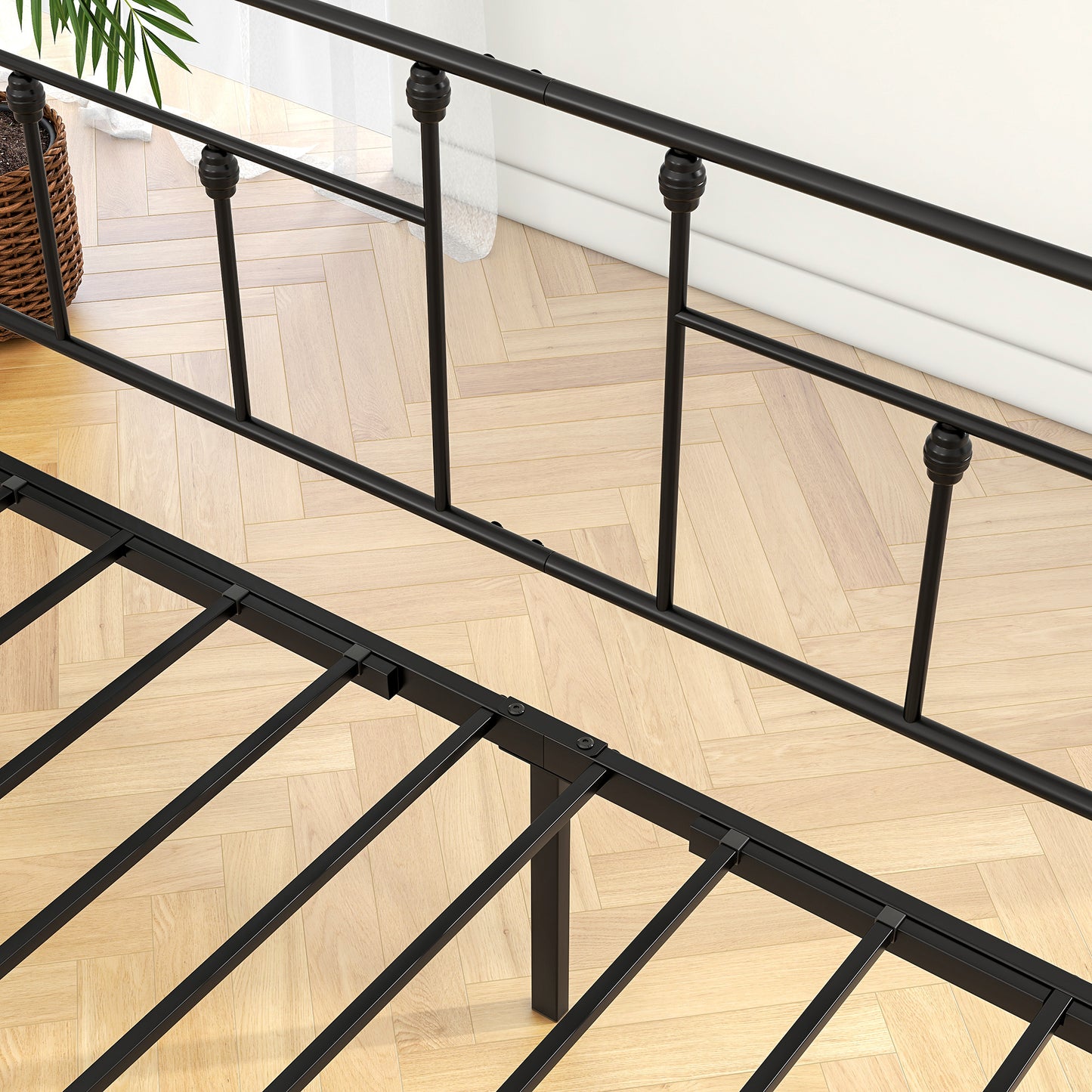 Closeup of black metal bed frame featuring ornate finials on vertical posts a sturdy base and wooden flooring