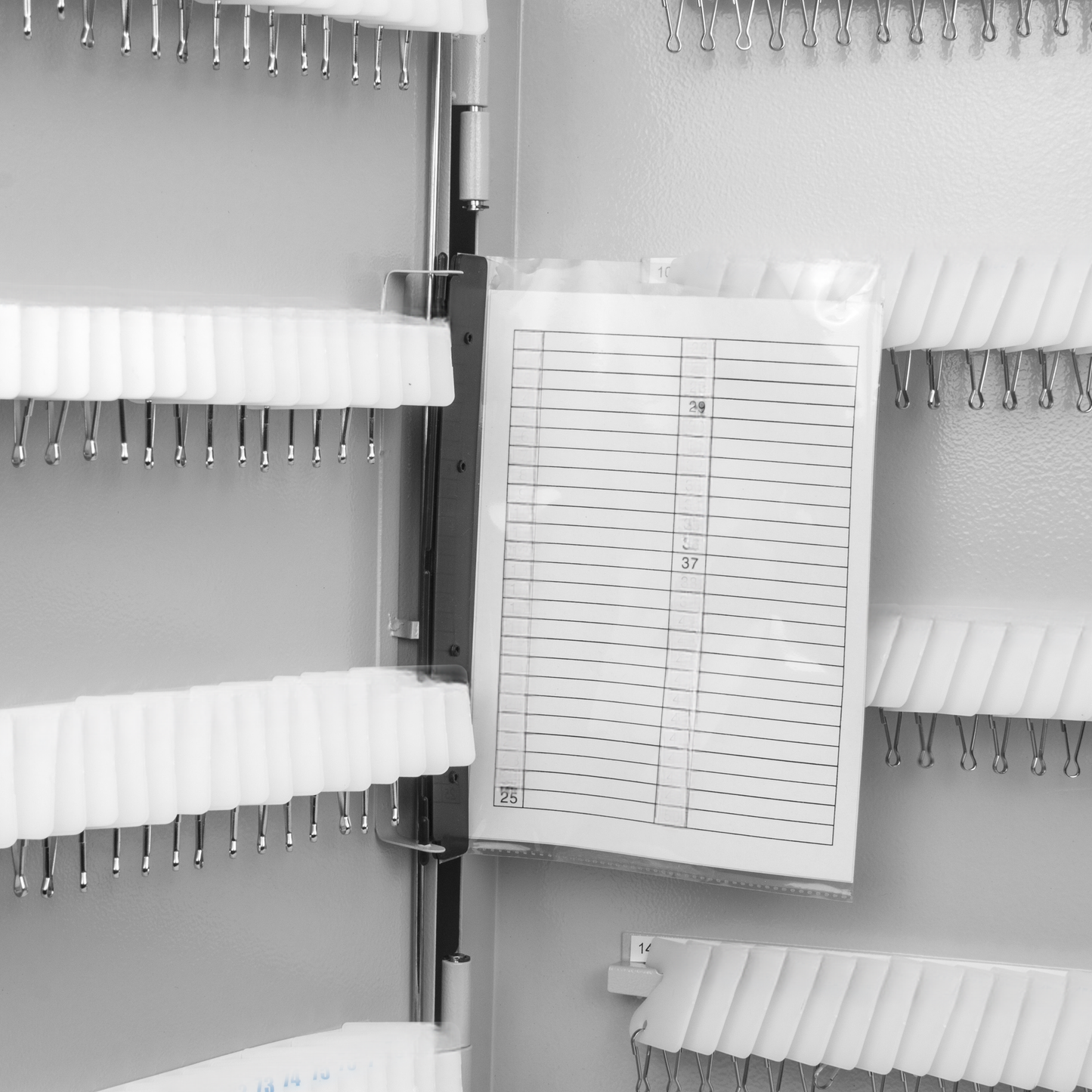 Gray metal key organizer with rows of white hooks and a clear plastic index card holder