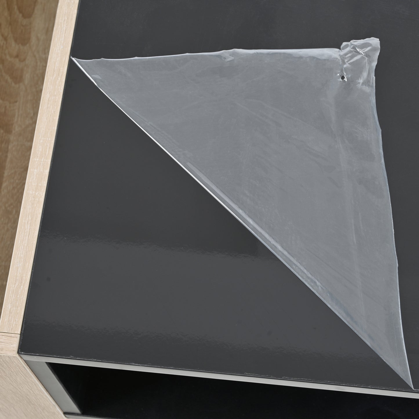 Clear protective film peeling off a glossy black tabletop showcasing furniture detail