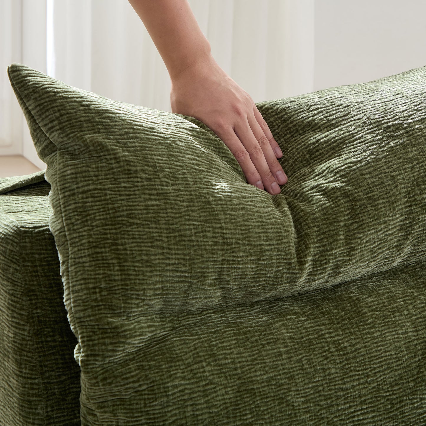 Textured green velvet sofa cushion with a hand gently pressing the fabric