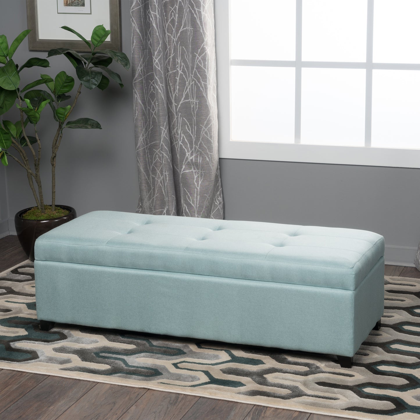 Tufted light blue storage ottoman with wooden legs on a geometric rug