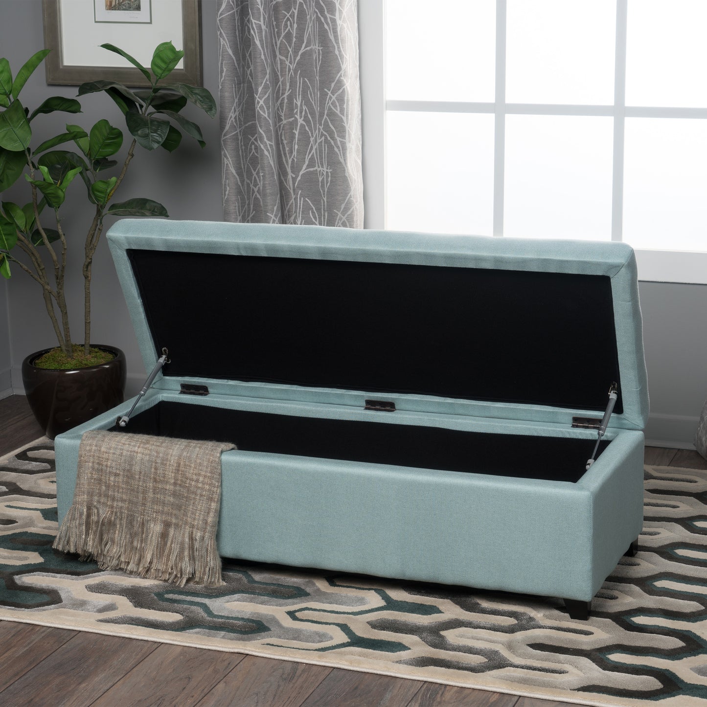 Light blue upholstered storage bench with open lid and a throw blanket