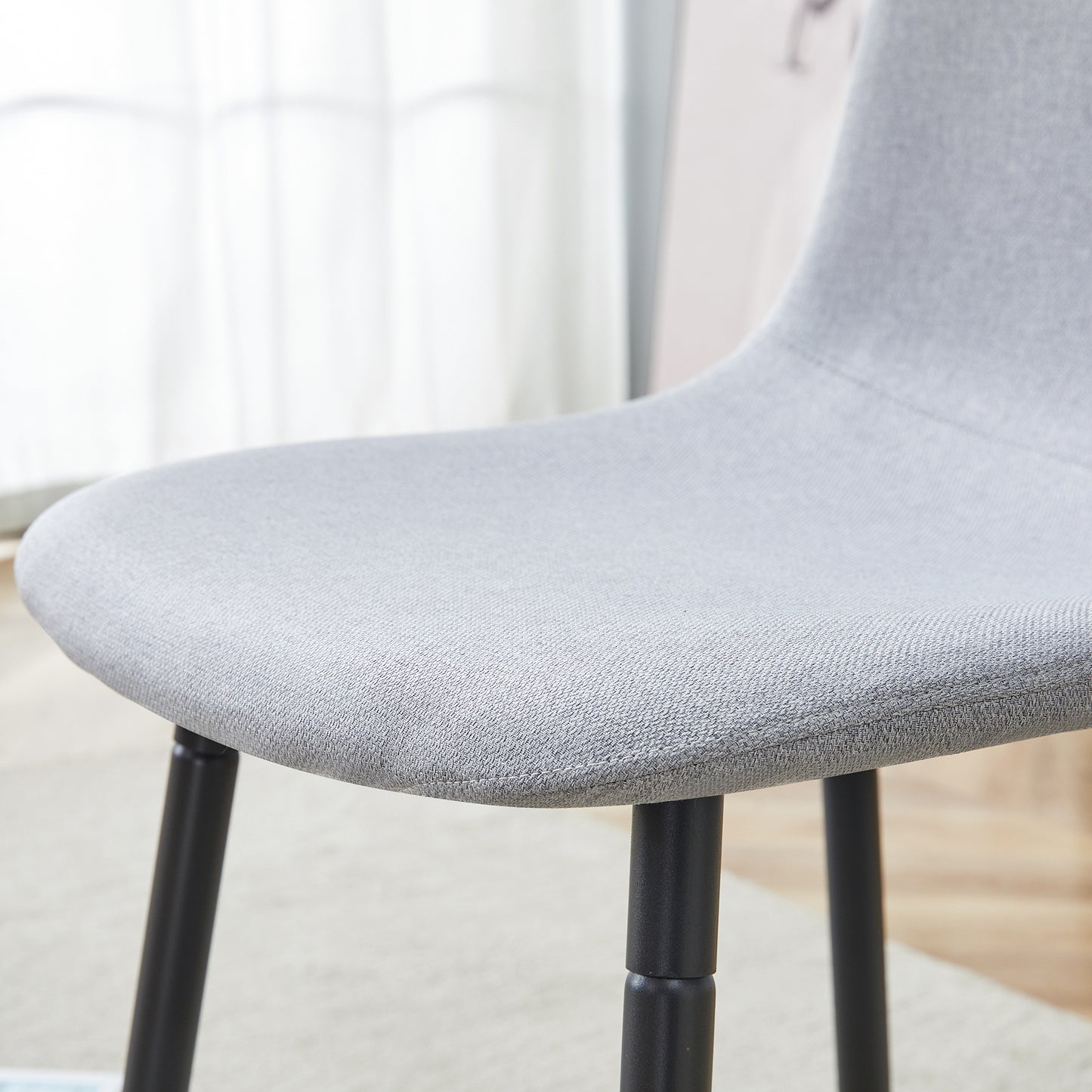 Close up of a grey fabric upholstered chair seat with black metal legs modern dining chair
