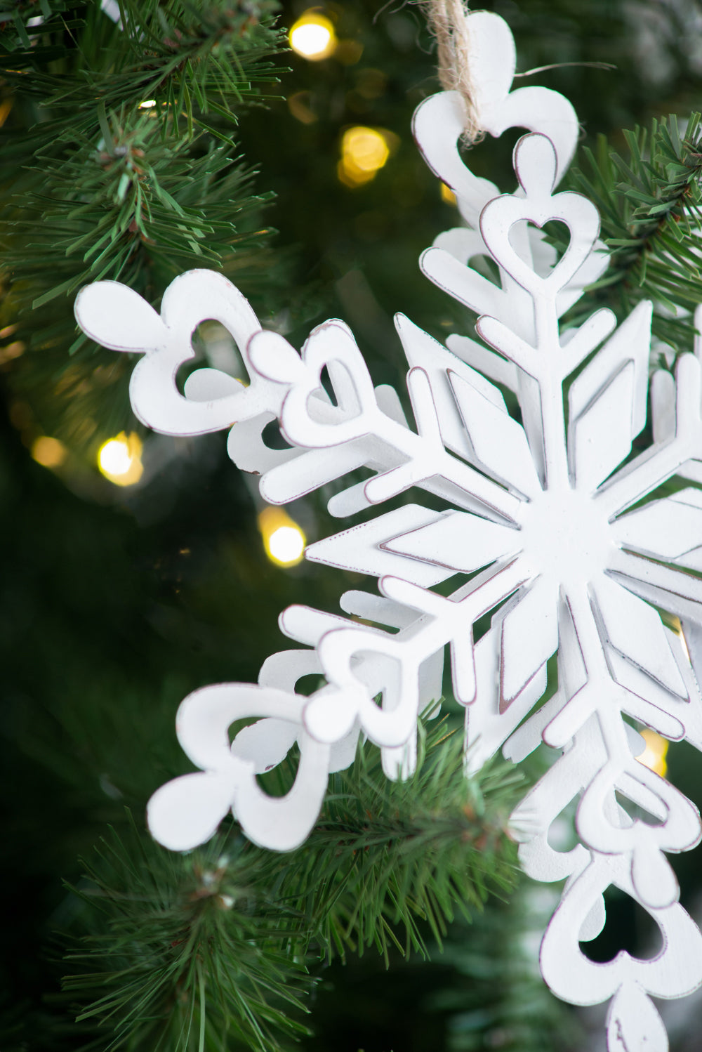 White distressed wooden snowflake ornament with heart cutouts hanging on a Christmas tree