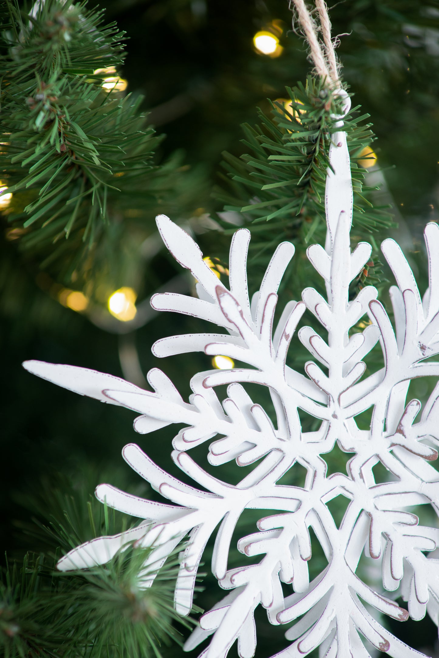 White distressed metal snowflake ornament hanging on a Christmas tree branch