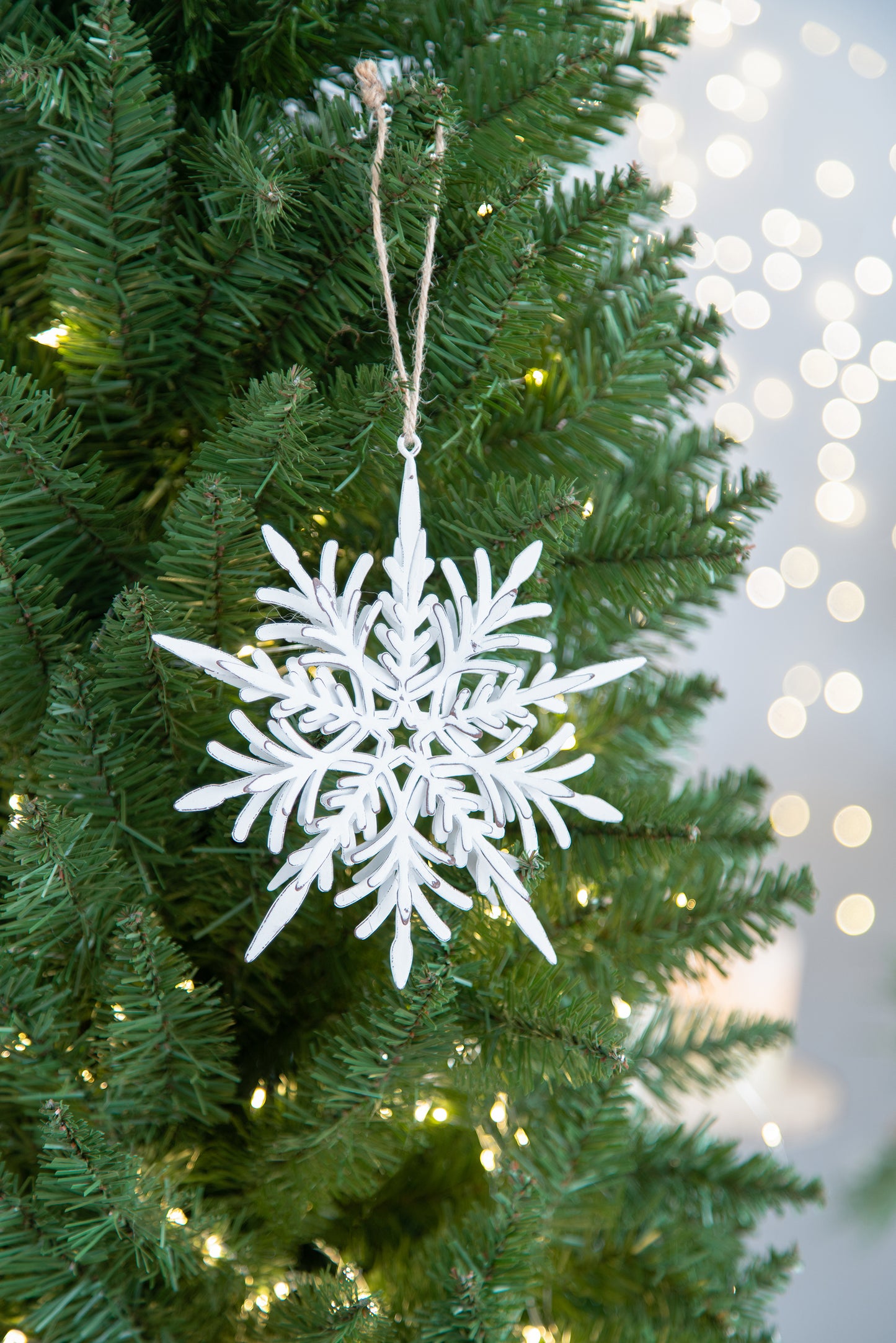 Rustic white metal snowflake ornament hanging on a Christmas tree with fairy lights