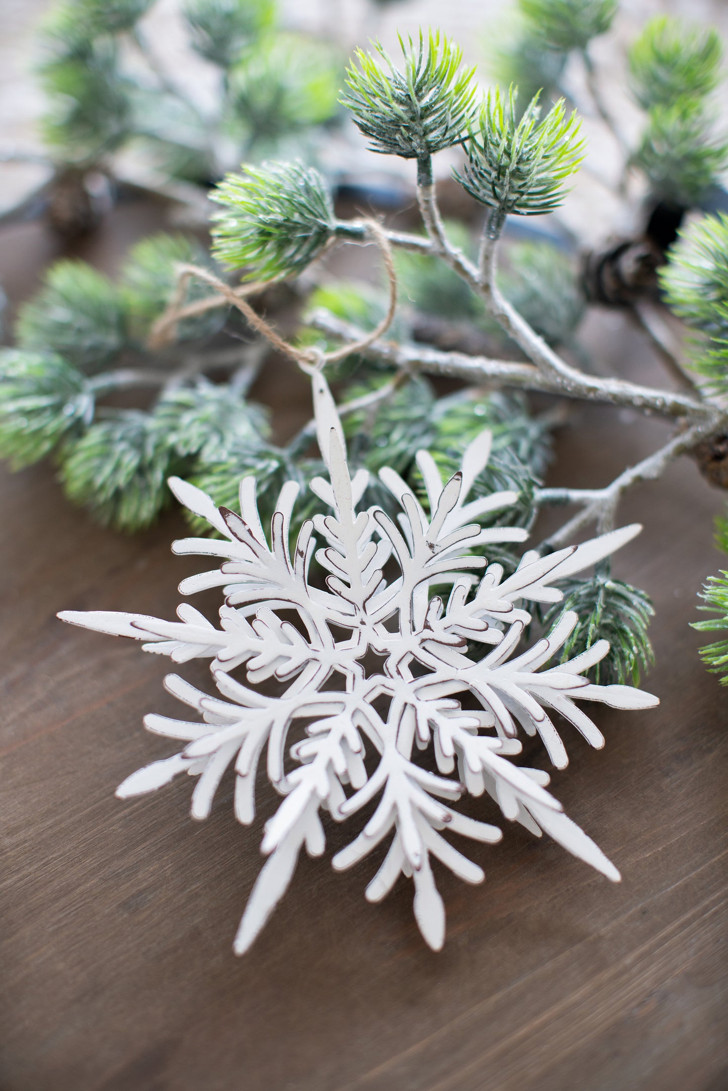 Rustic white metal snowflake ornament with distressed brown edges hanging from pine branch