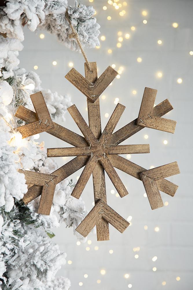 Rustic wooden snowflake ornament hanging on a flocked Christmas tree branch