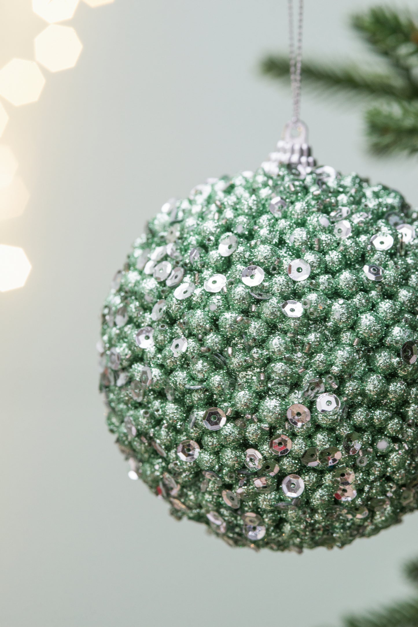Sparkling green Christmas bauble adorned with silver sequins hanging from a festive tree