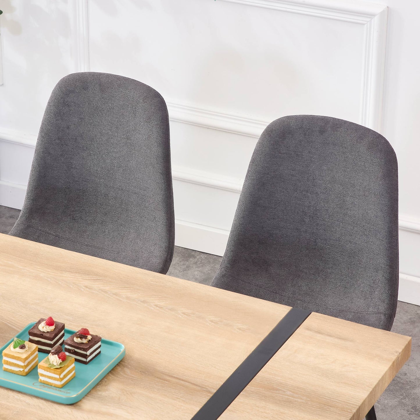 Two grey fabric dining chairs beside a light wood table with black accent