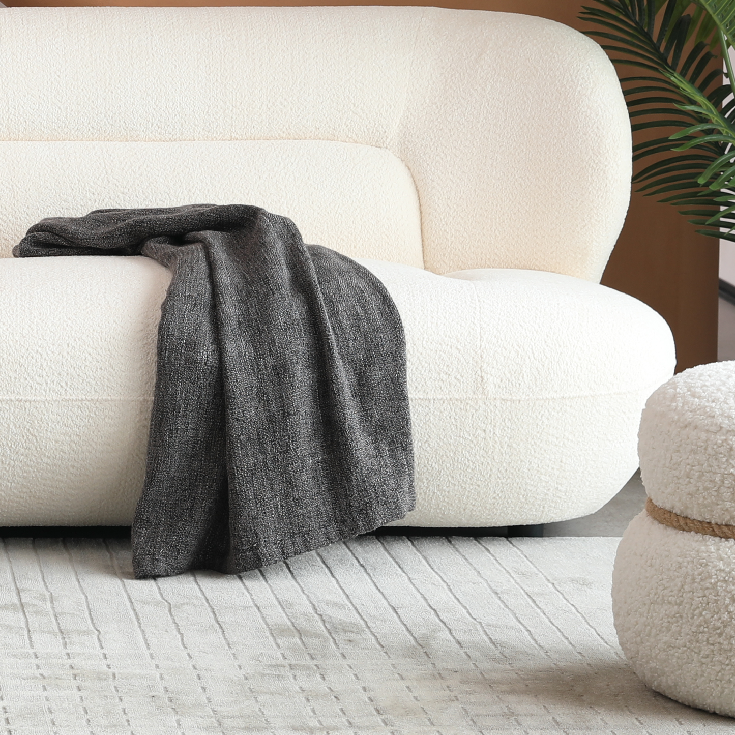 Plush ivory boucle sofa with a dark grey textured throw blanket draped over the armrest