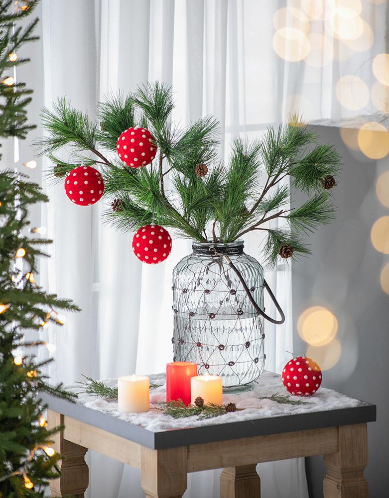 Festive red polka dot christmas ornaments hanging from pine branches in a wirewrapped glass vase