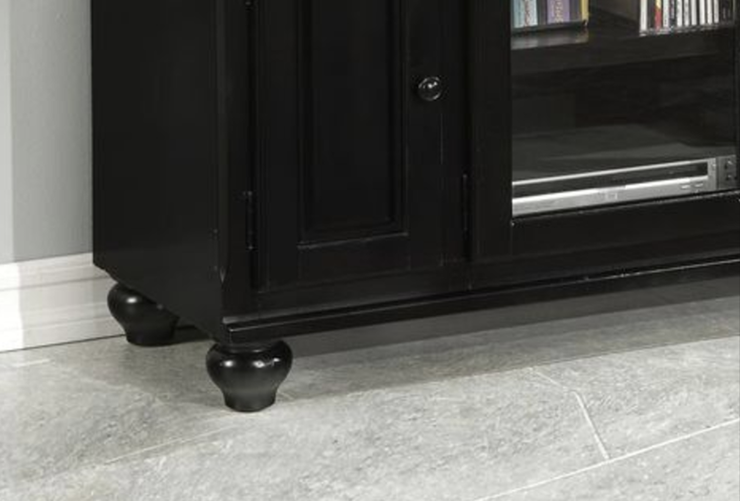 Black wooden media console with decorative bun feet holds media equipment and DVDs