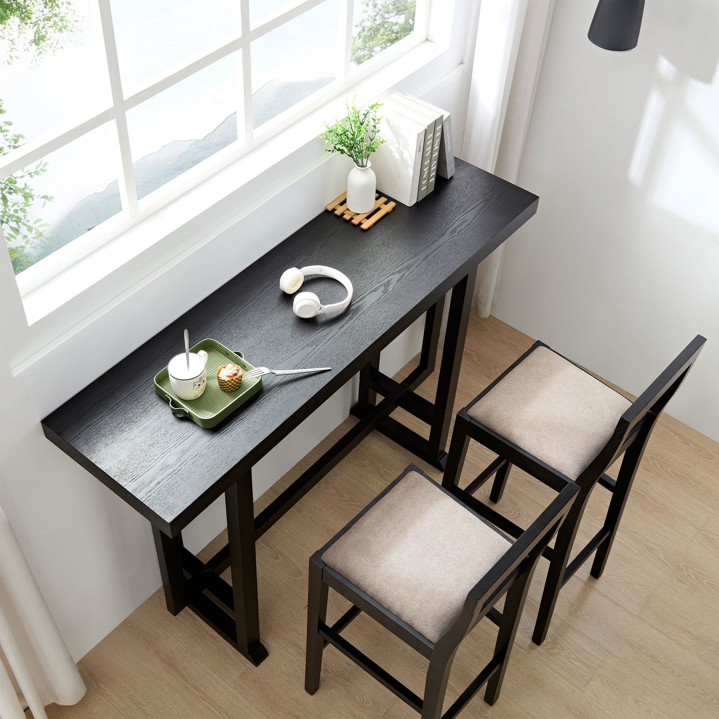 Black wood bar table with neutral upholstered stools and a small green tray