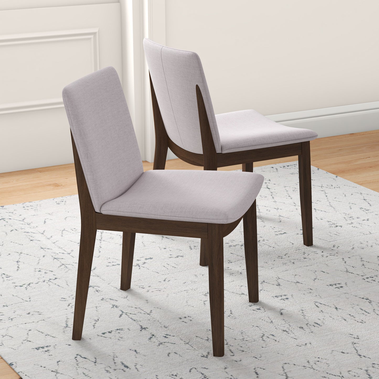 Two upholstered dining chairs with light grey fabric seats and dark wood legs on a patterned rug