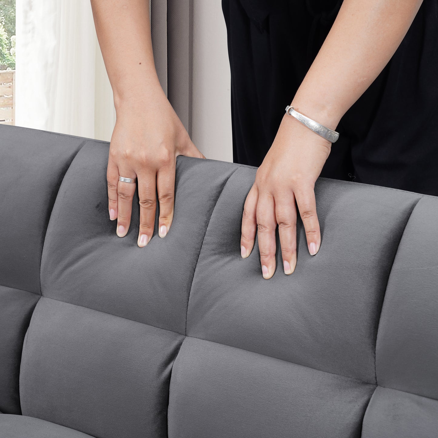 Hands pressing into tufted grey velvet sofa cushion showing comfort